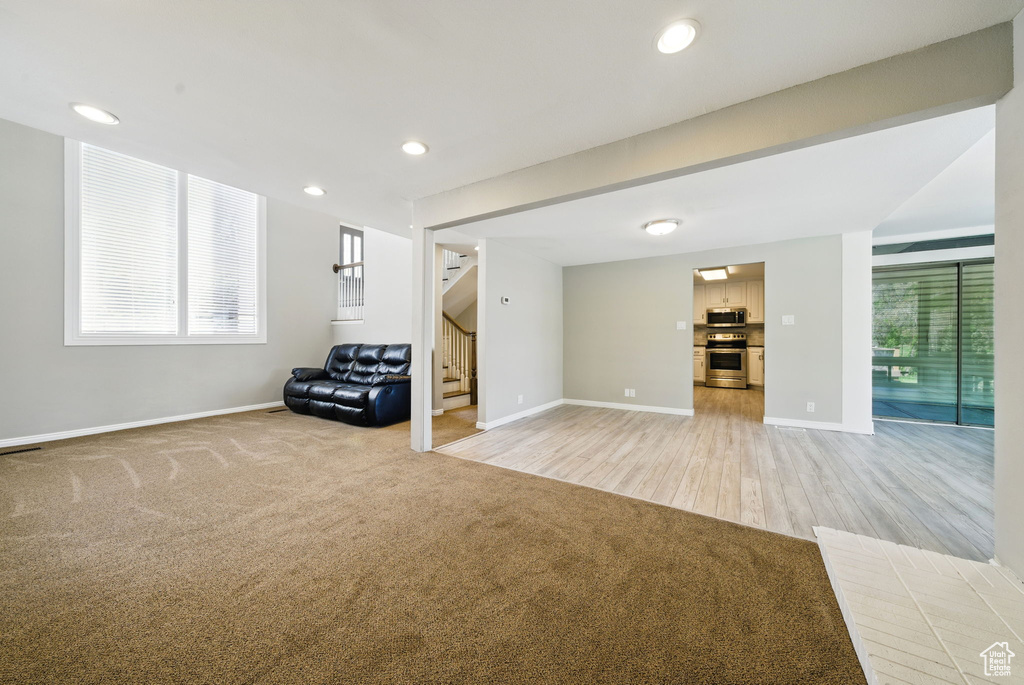 Below grade area with stairway, baseboards, light colored carpet, plenty of natural light, and recessed lighting