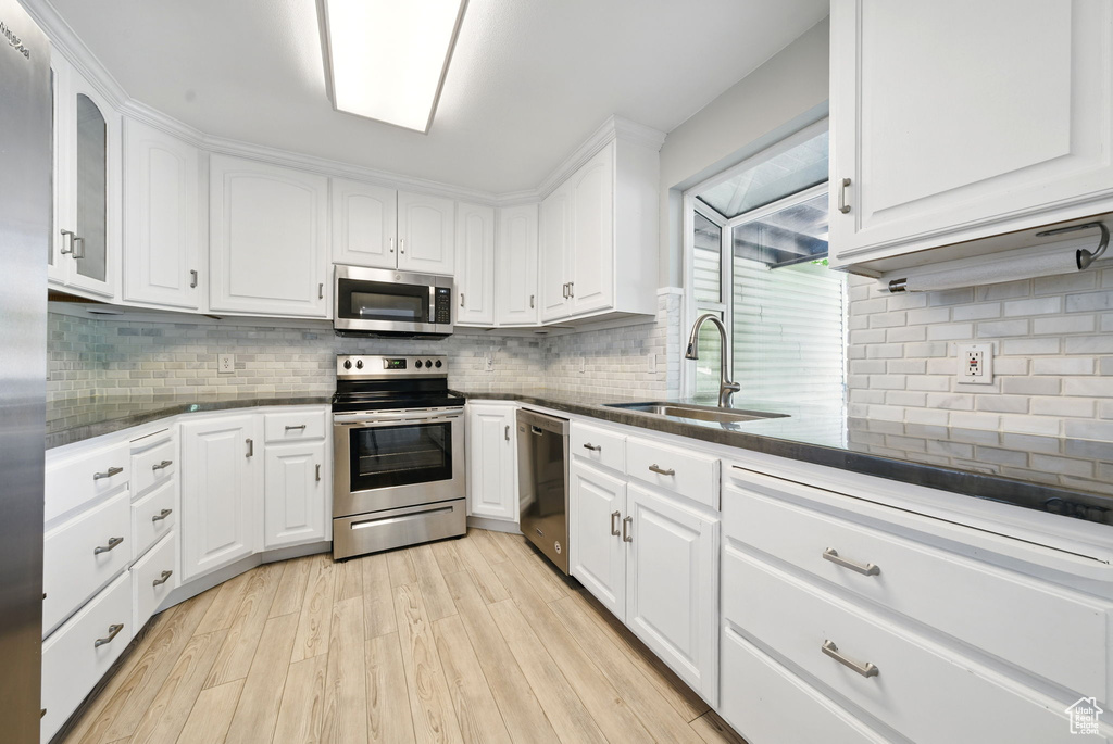 Kitchen with appliances with stainless steel finishes, a sink, tasteful backsplash, and white cabinets