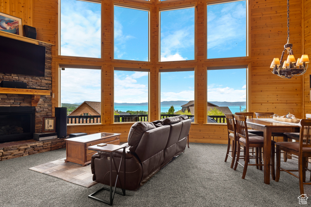 Carpeted living room featuring a water view, a chandelier, wooden walls, a stone fireplace, and a towering ceiling