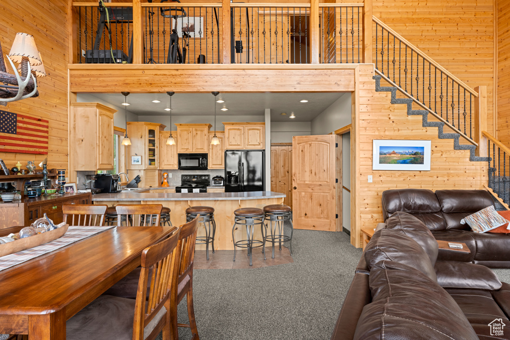 Dining space featuring wood walls, a high ceiling, stairway, and dark carpet
