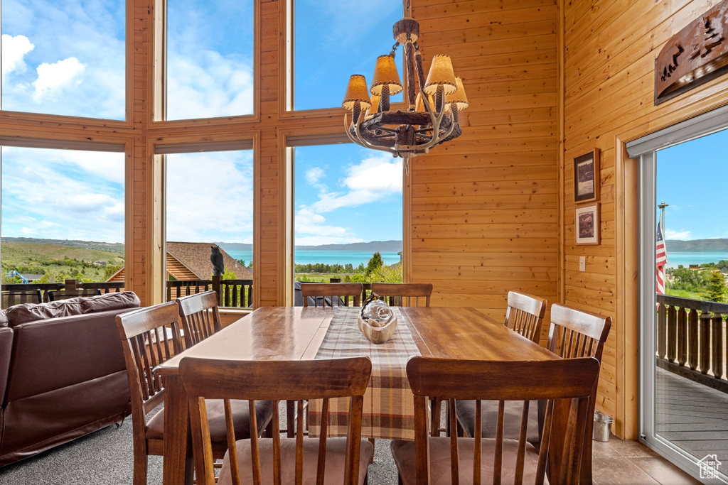 Dining space featuring a chandelier, plenty of natural light, a water view, wood walls, and a towering ceiling