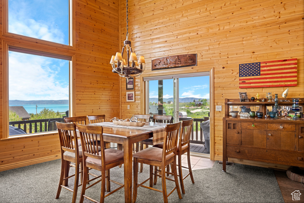 Carpeted dining space featuring wood walls, a chandelier, plenty of natural light, a water view, and a high ceiling