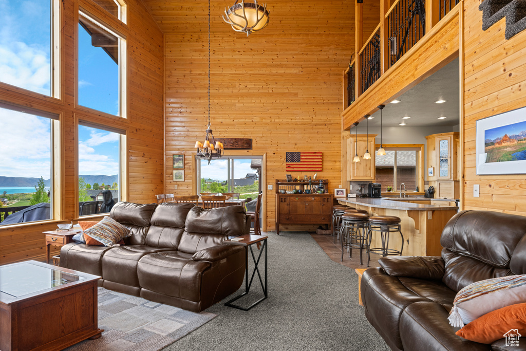Living area with a high ceiling, wooden walls, a chandelier, and carpet floors