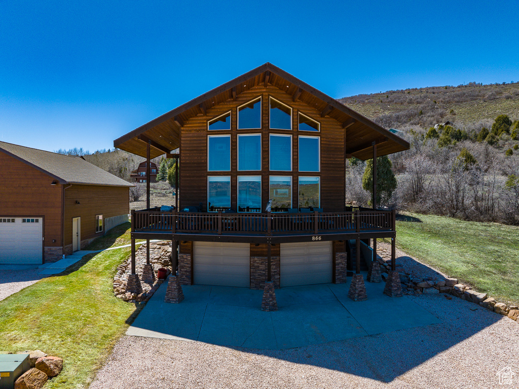 View of front facade featuring stone siding, a front lawn, a deck, a garage, and driveway