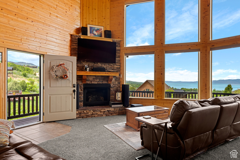 Carpeted living room featuring wooden walls, a towering ceiling, a stone fireplace, and tile patterned floors