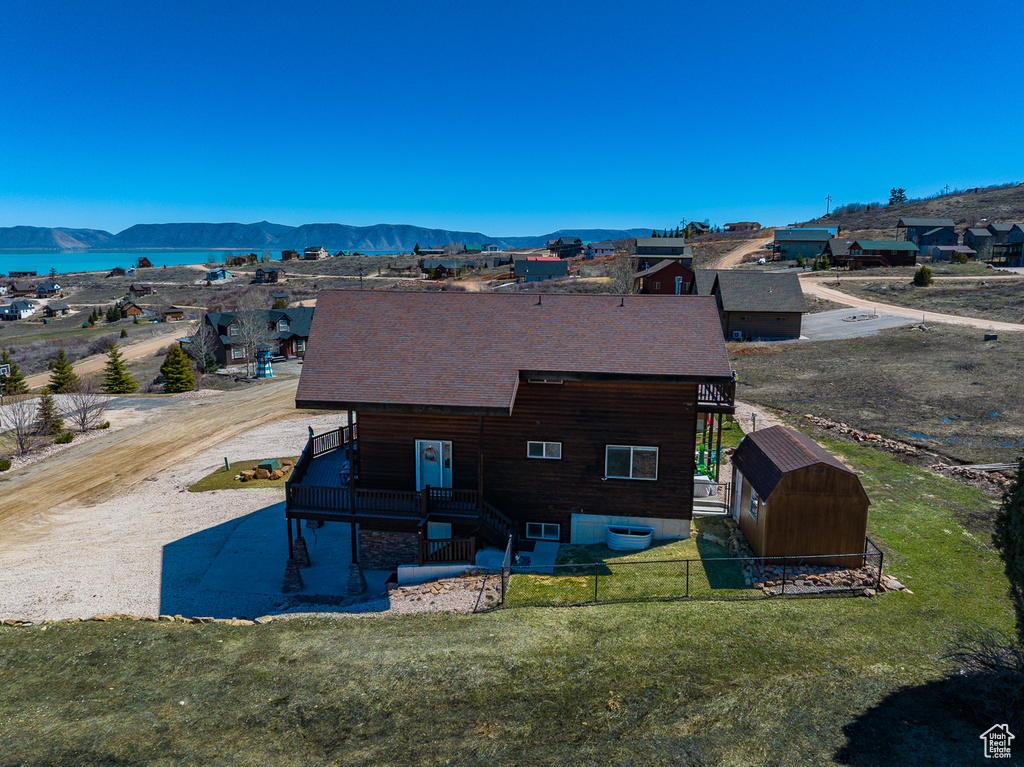 Back of property featuring a storage shed, an outbuilding, a deck with water view, a yard, and roof with shingles