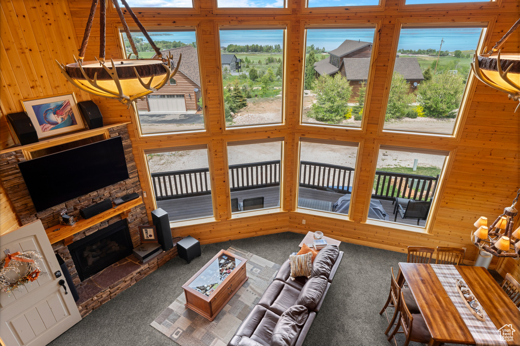 Living area featuring carpet, plenty of natural light, a stone fireplace, wood walls, and a high ceiling