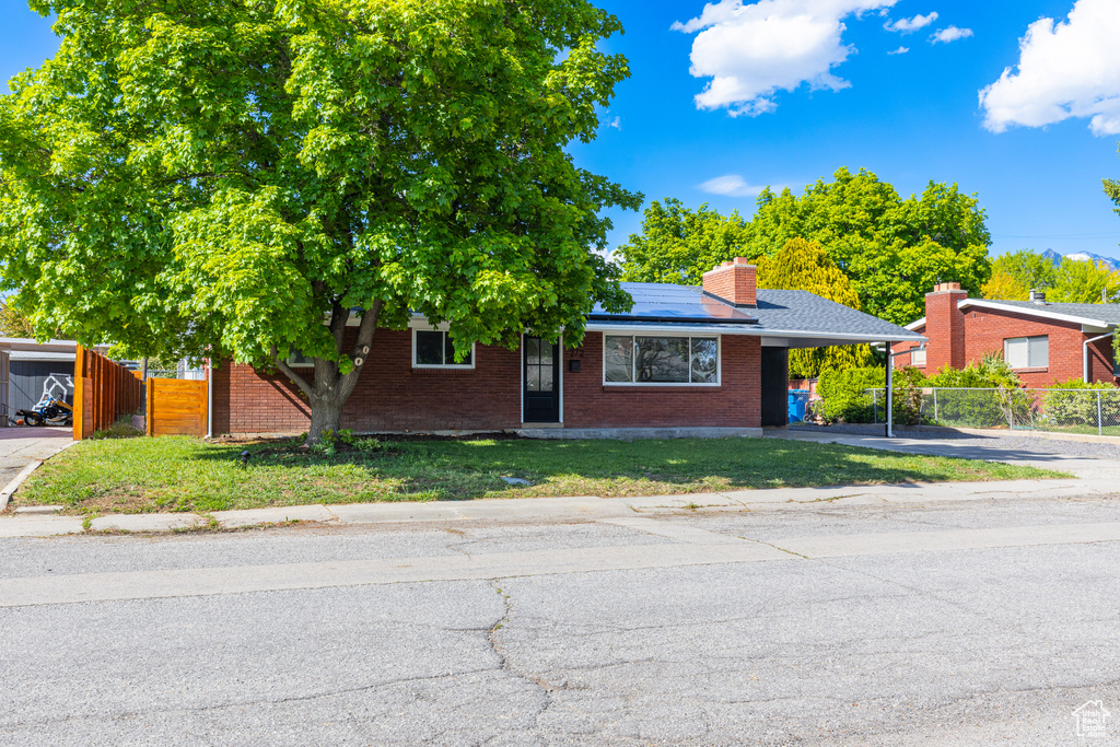View of front of house featuring solar panels, brick siding, a carport, a chimney, and driveway