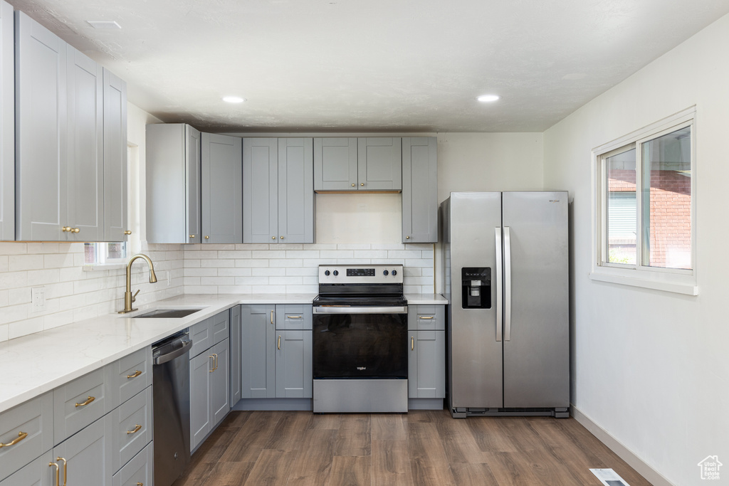Kitchen featuring appliances with stainless steel finishes, a sink, gray cabinets, dark wood-style flooring, and tasteful backsplash