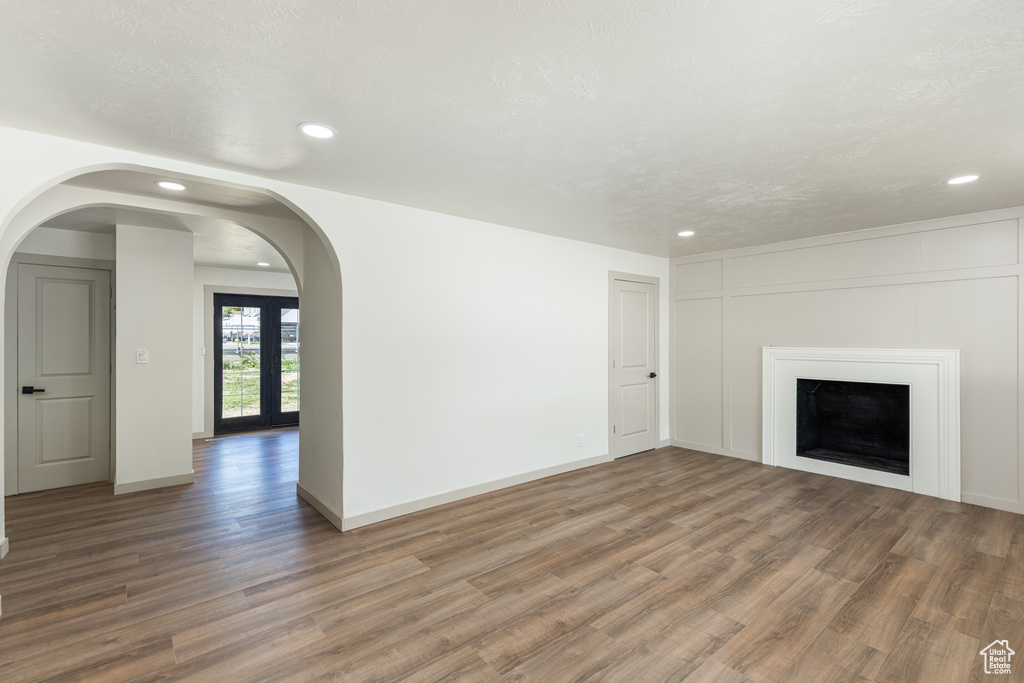 Unfurnished living room featuring recessed lighting, wood finished floors, a fireplace, arched walkways, and baseboards