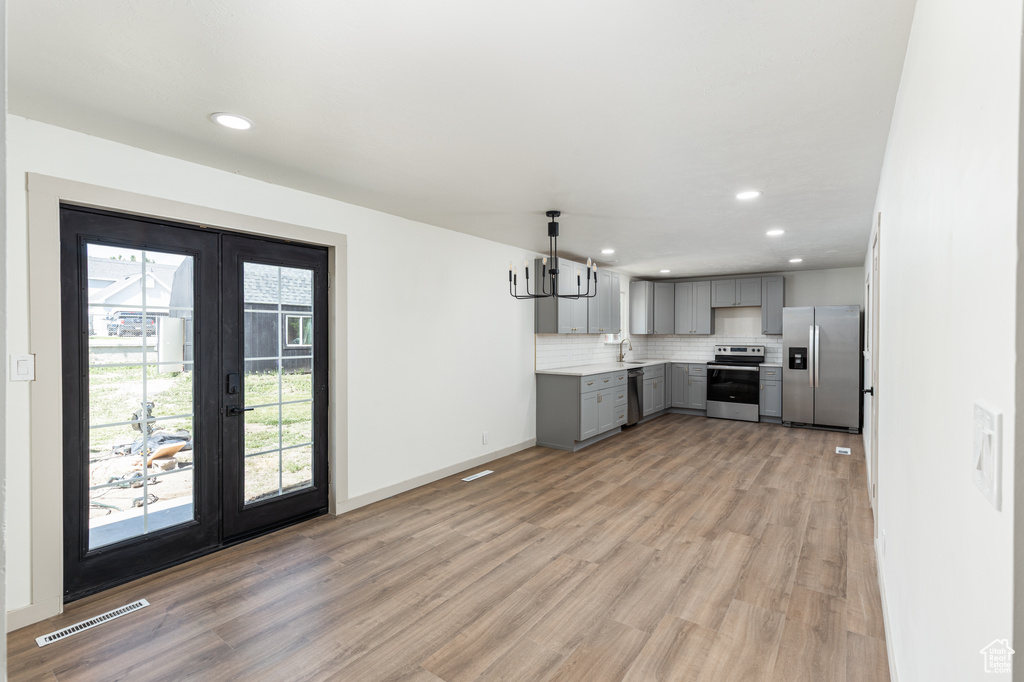 Kitchen with appliances with stainless steel finishes, gray cabinets, french doors, a sink, and light wood-style floors