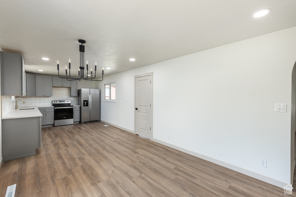 Kitchen with appliances with stainless steel finishes, gray cabinetry, light countertops, a chandelier, and light wood-style floors