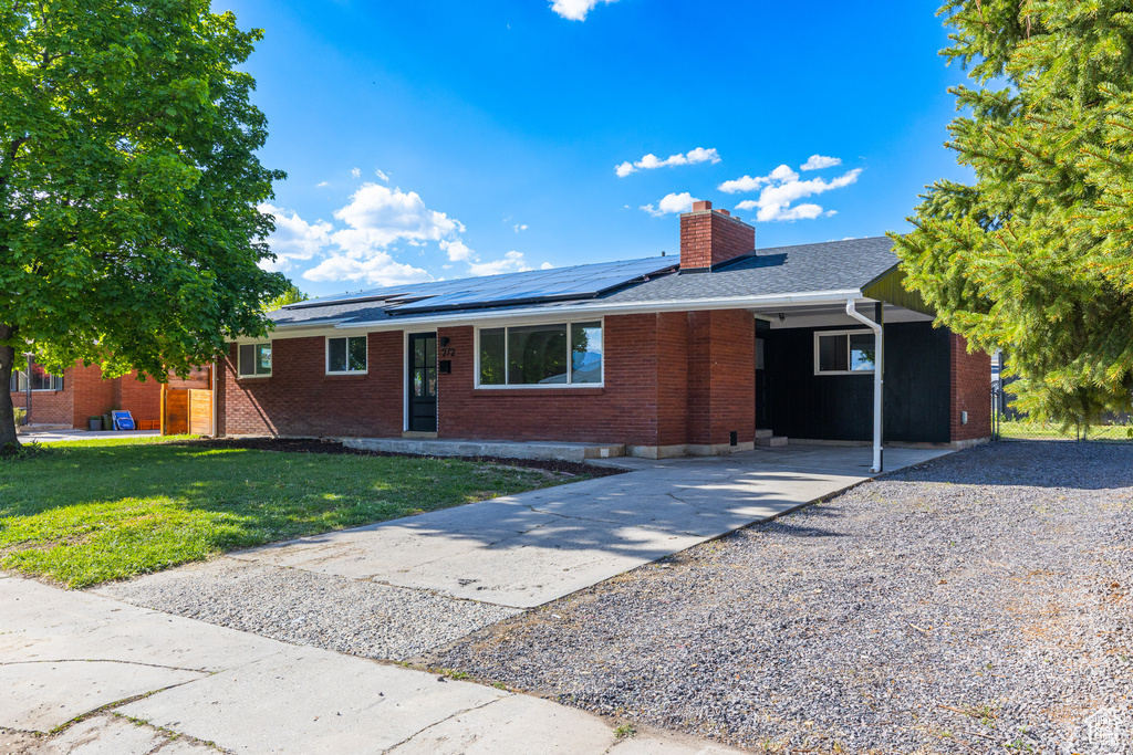 Single story home featuring brick siding, concrete driveway, a chimney, a front lawn, and solar panels