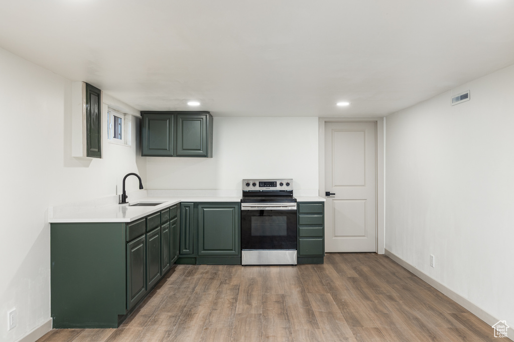 Kitchen with electric range, a sink, green cabinetry, wood finished floors, and light countertops