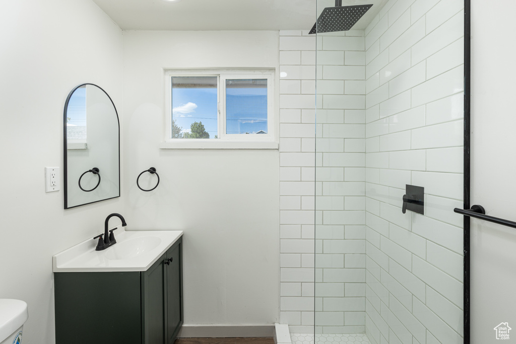 Bathroom featuring a tile shower, toilet, and vanity
