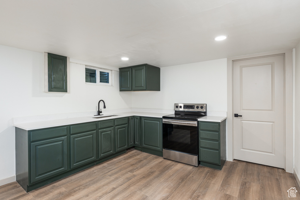 Kitchen with electric stove, green cabinets, a sink, and recessed lighting