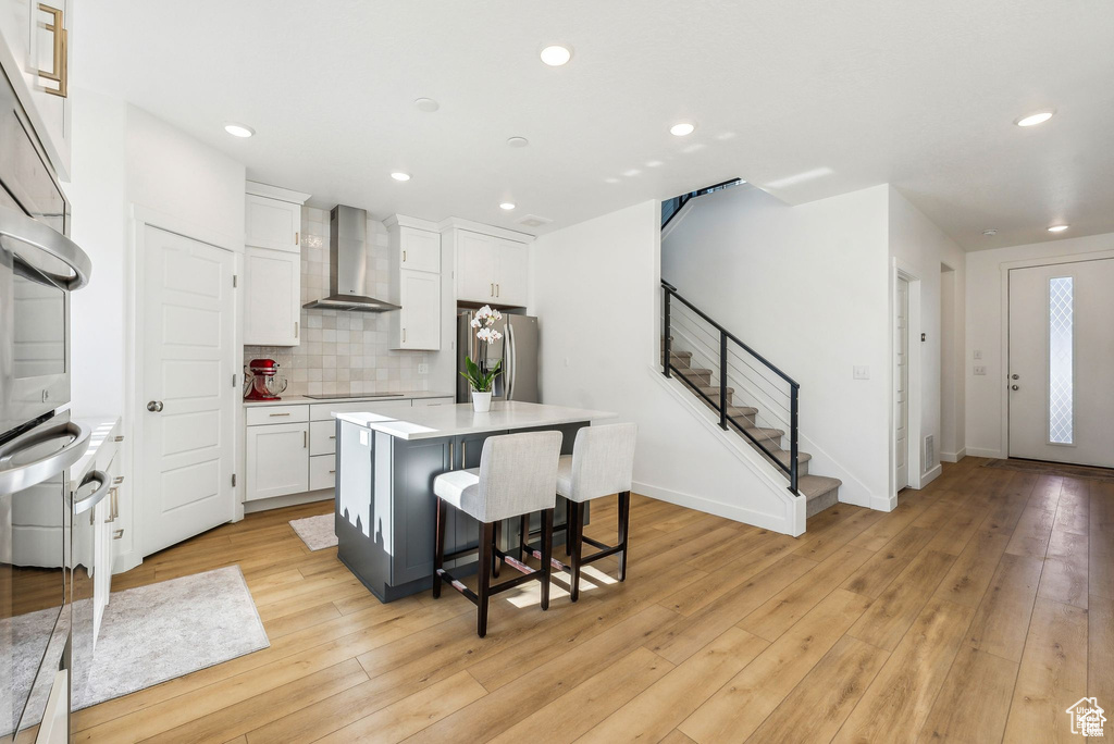 Kitchen with wall chimney exhaust hood, stainless steel appliances, a center island, white cabinets, and recessed lighting