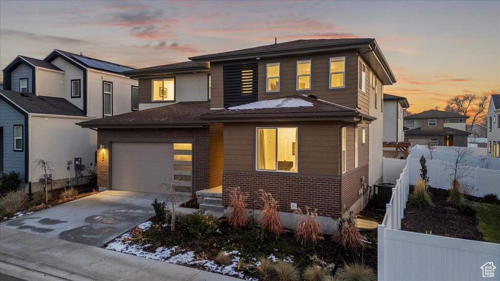 View of front of property with driveway, a garage, fence, brick siding, and central AC unit