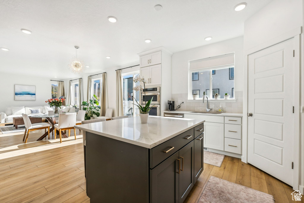 Kitchen with a sink, open floor plan, stainless steel double oven, white cabinetry, and decorative backsplash