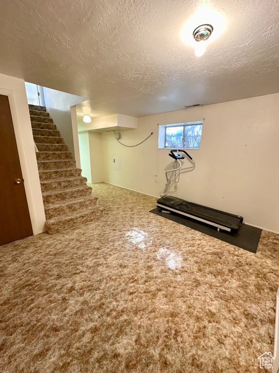 Below grade area with carpet flooring, a textured ceiling, and stairway