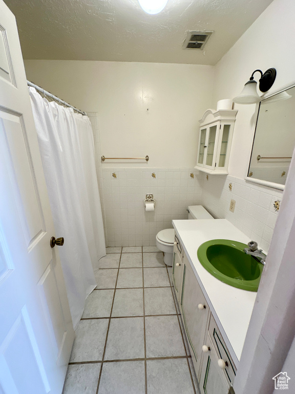 Full bathroom with tile patterned floors, toilet, vanity, tile walls, and wainscoting