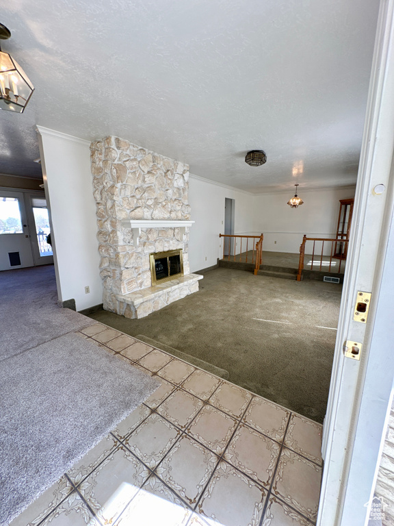 Unfurnished living room featuring carpet floors, a chandelier, baseboards, crown molding, and a fireplace