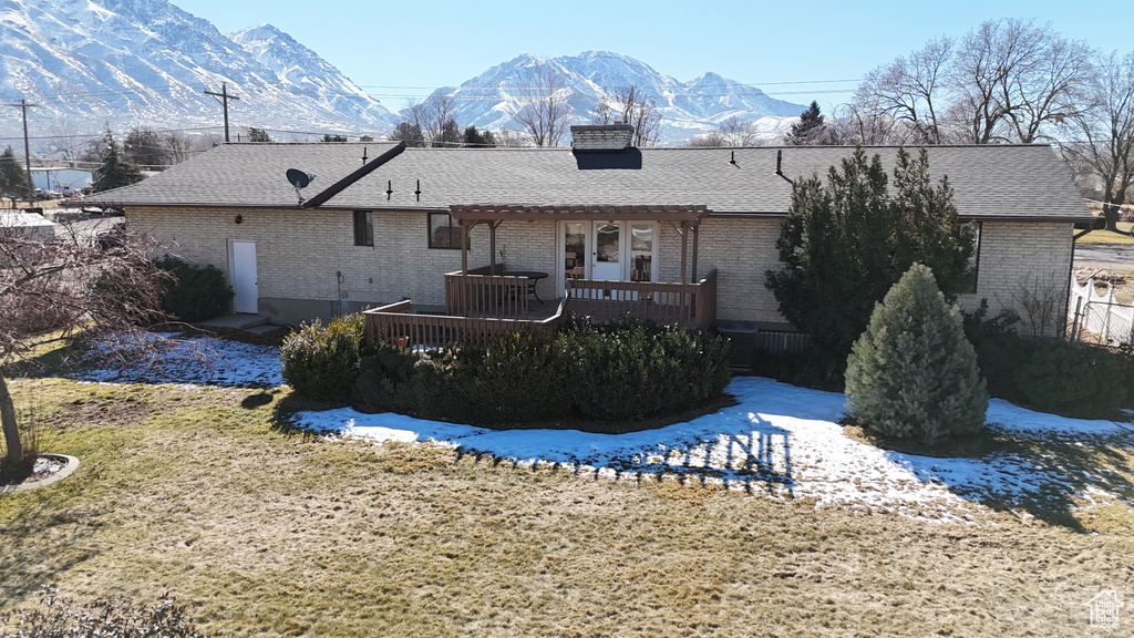 Back of property with brick siding, a deck with mountain view, and roof with shingles