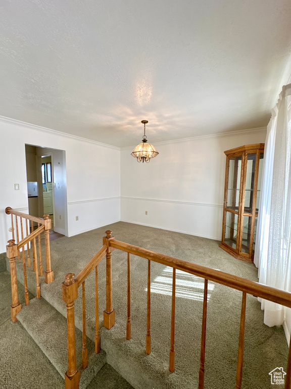 Spare room with carpet flooring, a chandelier, crown molding, and stairway