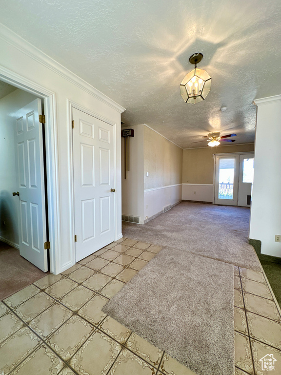 Unfurnished living room featuring light colored carpet, a textured ceiling, ornamental molding, and ceiling fan