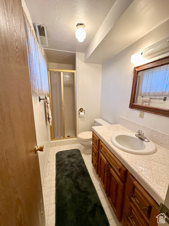Bathroom featuring a stall shower, vanity, toilet, and a textured ceiling