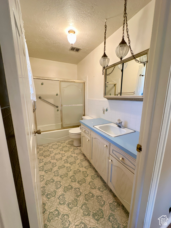 Full bathroom with toilet, vanity, a textured ceiling, and bath / shower combo with glass door