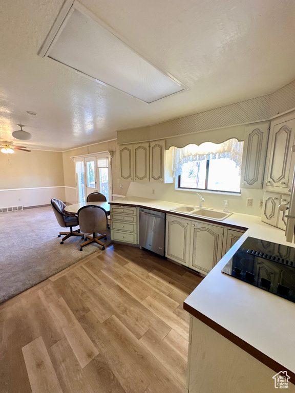 Kitchen with stainless steel dishwasher, a sink, light wood-style floors, and light countertops