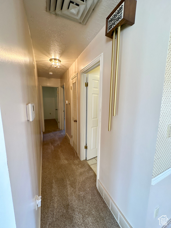 Hallway with light carpet, a textured ceiling, and baseboards