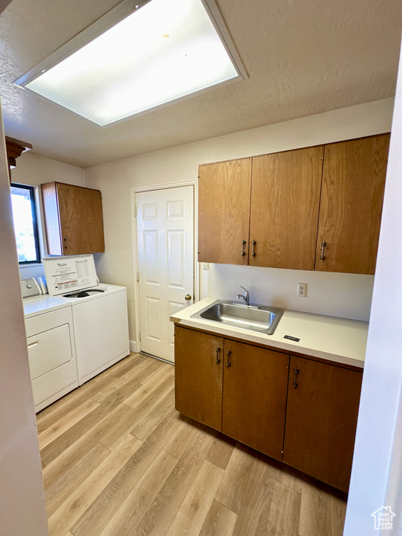 Kitchen with a sink, washing machine and clothes dryer, light wood-style flooring, light countertops, and brown cabinets