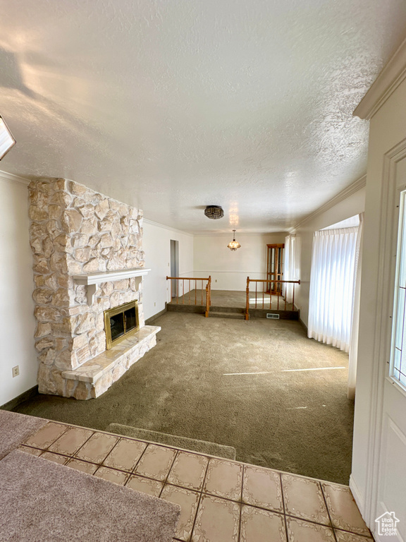 Unfurnished living room with carpet flooring, a textured ceiling, crown molding, a stone fireplace, and a chandelier