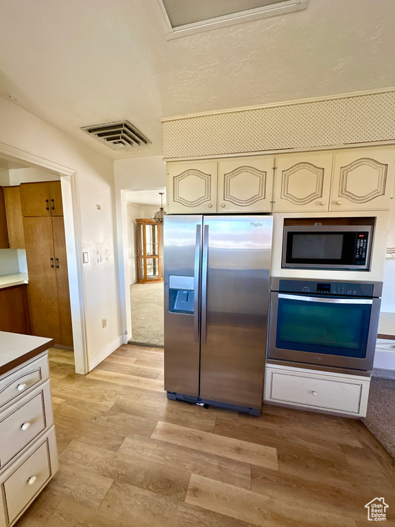 Kitchen featuring appliances with stainless steel finishes, cream cabinetry, light wood-style flooring, light countertops, and baseboards