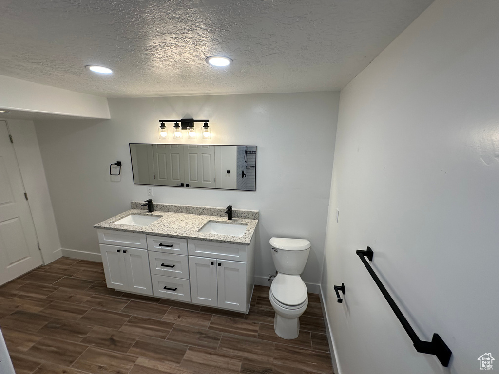 Full bathroom with baseboards, wood finish floors, toilet, a textured ceiling, and double vanity