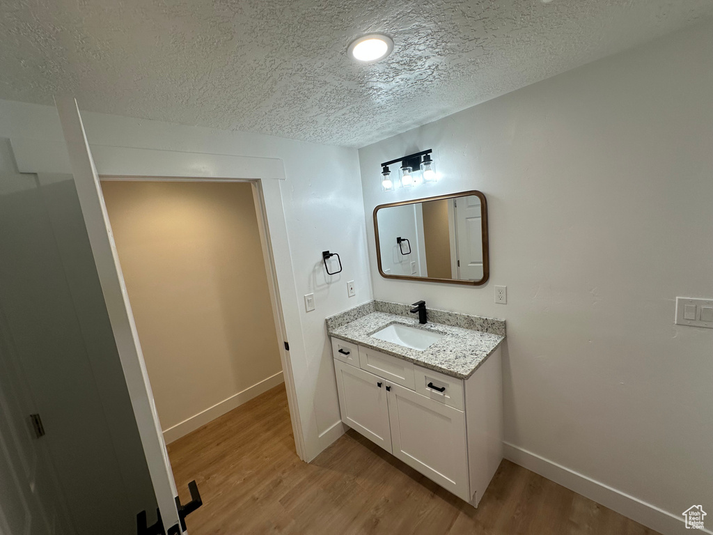 Bathroom with a textured ceiling, wood finished floors, vanity, baseboards, and recessed lighting