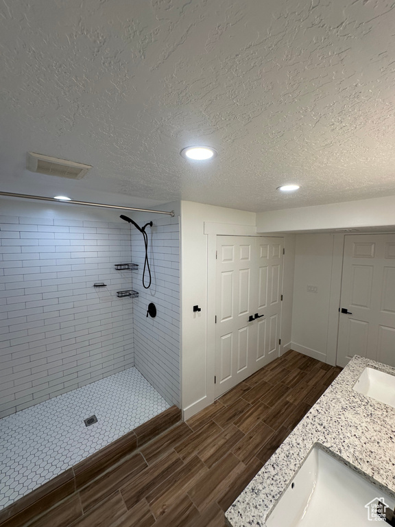 Bathroom with a textured ceiling, a tile shower, wood finish floors, recessed lighting, and baseboards
