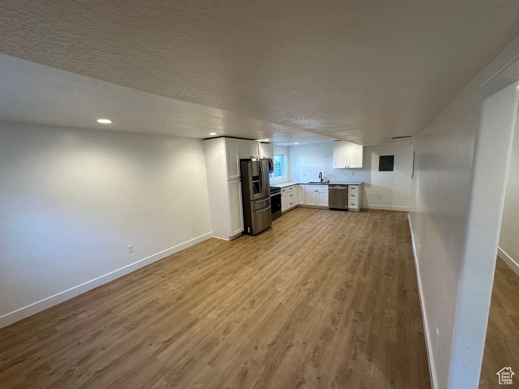 Unfurnished living room featuring a sink, light wood-type flooring, baseboards, recessed lighting, and a textured ceiling