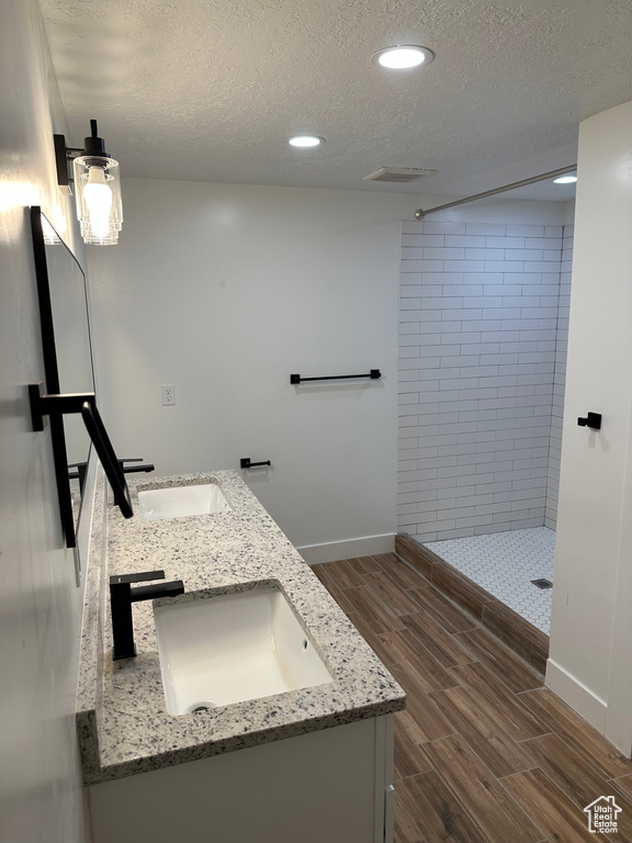 Full bathroom with wood finish floors, a tile shower, double vanity, a textured ceiling, and baseboards
