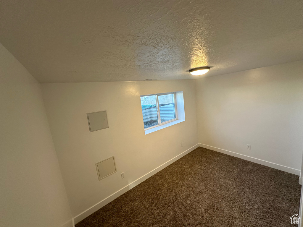 Spare room with dark carpet, baseboards, and a textured ceiling