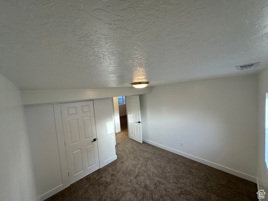 Unfurnished bedroom featuring dark colored carpet, baseboards, a textured ceiling, and a closet