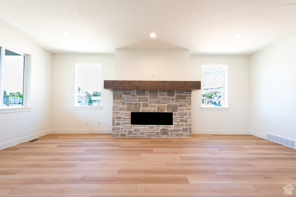 Unfurnished living room featuring light wood-style flooring, a stone fireplace, and recessed lighting