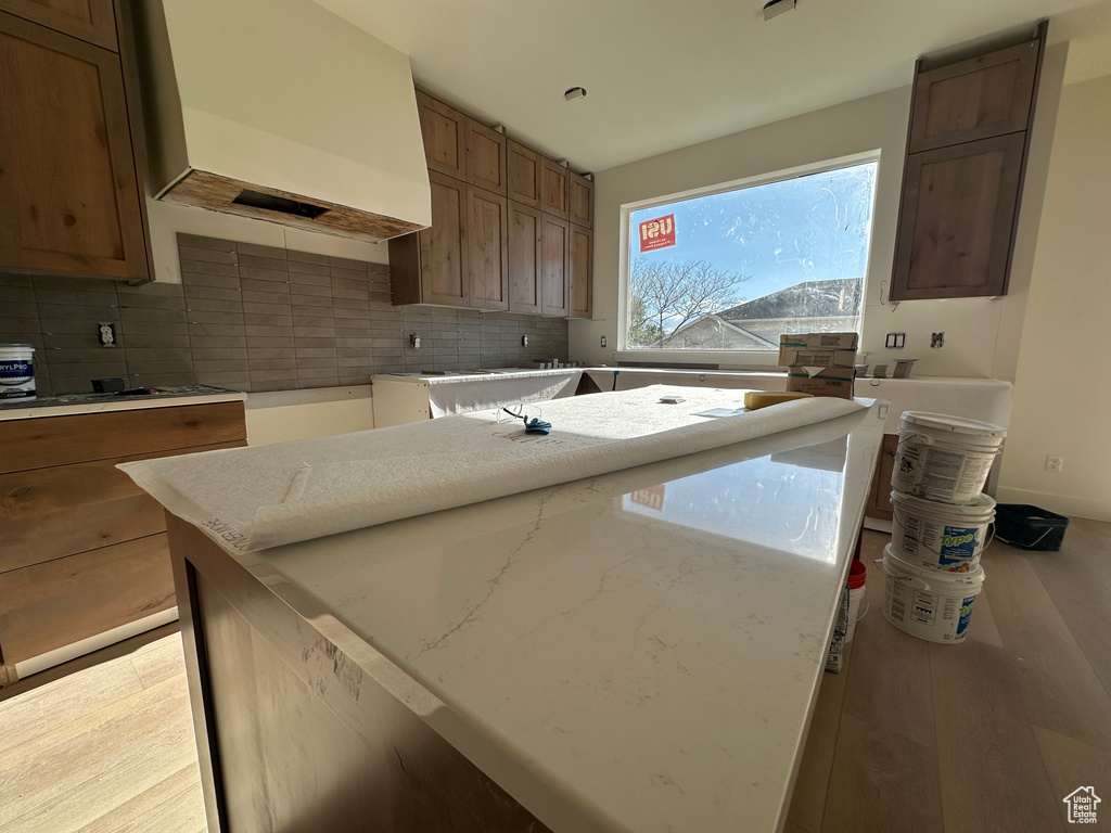 Kitchen with custom range hood, tasteful backsplash, light stone countertops, and wood finished floors