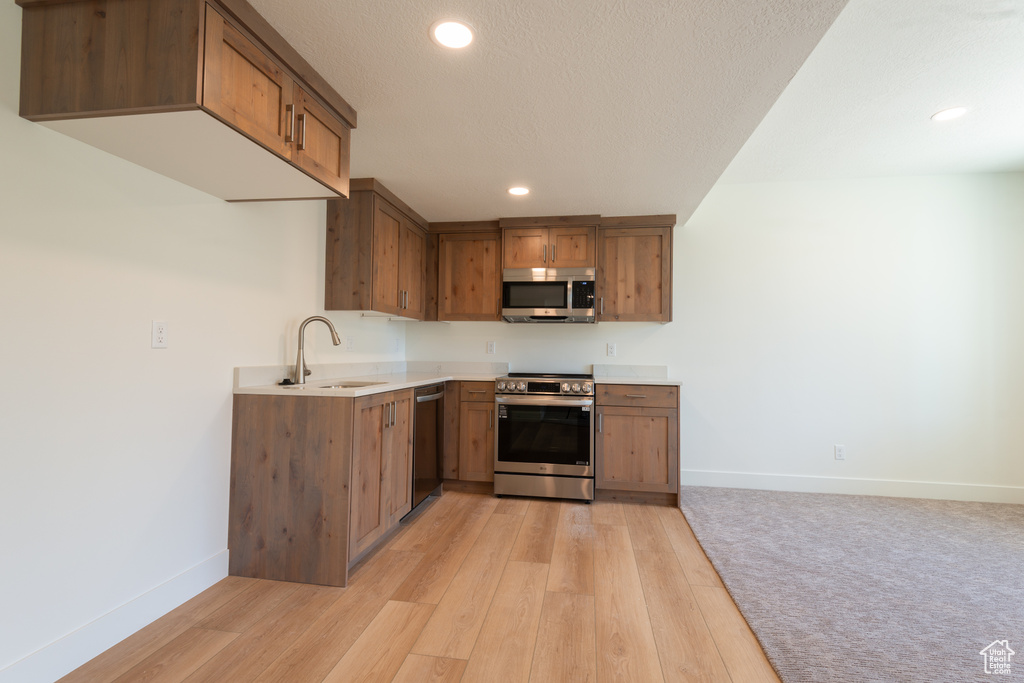 Kitchen featuring stainless steel appliances, brown cabinets, recessed lighting, light wood-style flooring, and light countertops