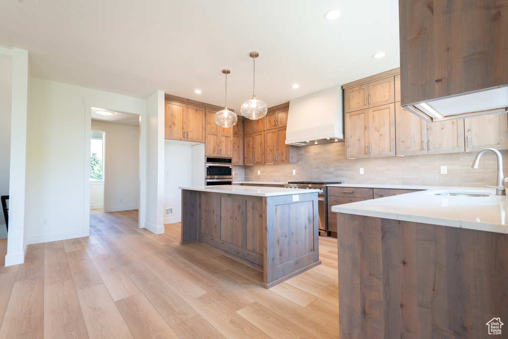 Kitchen with custom exhaust hood, stainless steel appliances, decorative backsplash, light wood-type flooring, and recessed lighting