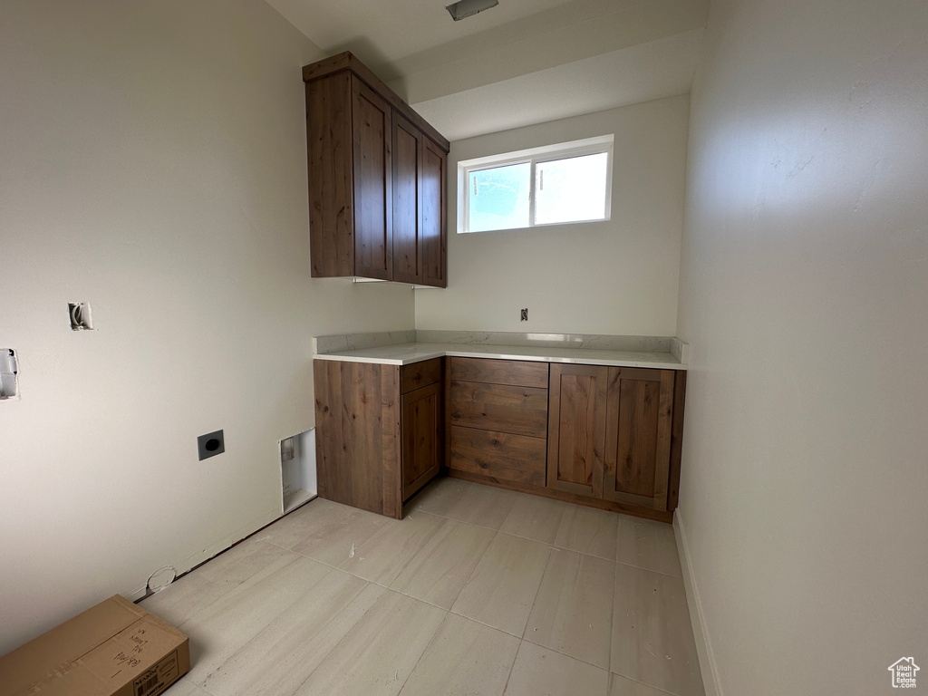 Clothes washing area with electric dryer hookup, light tile patterned flooring, cabinet space, and baseboards