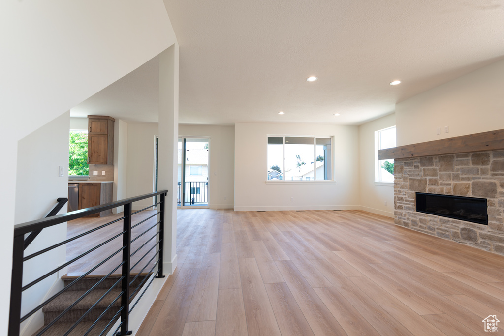 Unfurnished living room featuring light wood-style flooring, plenty of natural light, a stone fireplace, and recessed lighting