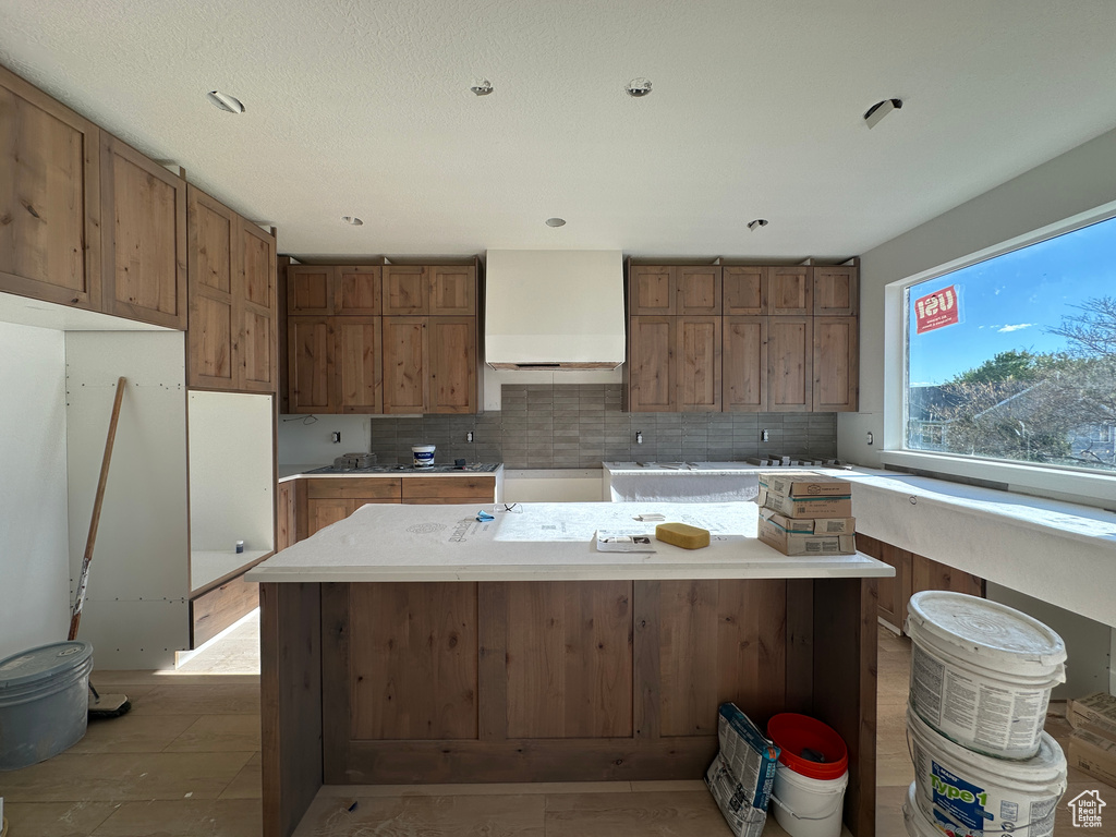 Kitchen featuring wall chimney range hood, brown cabinetry, backsplash, and a center island